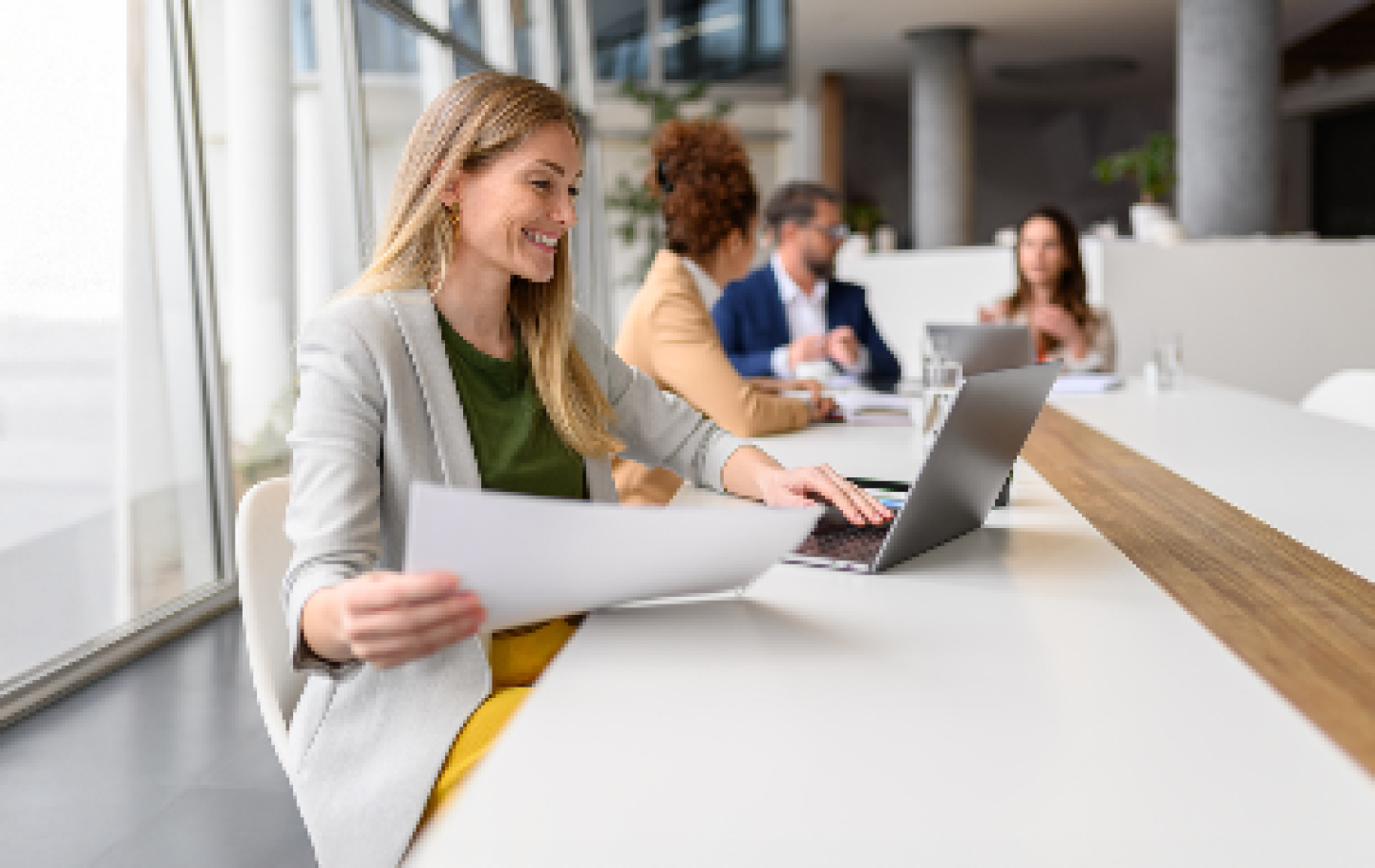 woman sitting in a conference room looking comparing paperwork to her screen