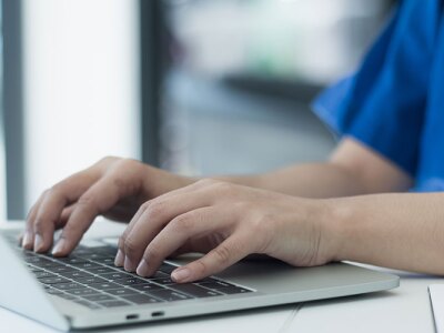 A healthcare professional is typing on a laptop, updating medical records, and conducting research.