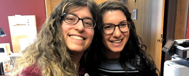 two-women-smiling-glasses-red-wall-background