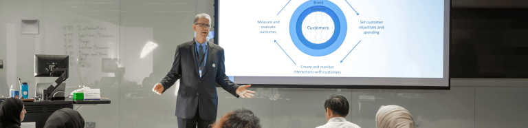 Man in suit delivering lecture to class in front of projector screen