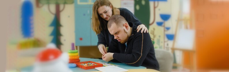 A female psychologist works with an adult boy with autism in the office.