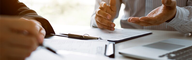 close up image of two sets of hands over paperwork and a laptop