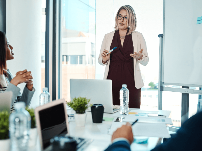 Woman at a whiteboard in front of a meeting room, leading a discussion