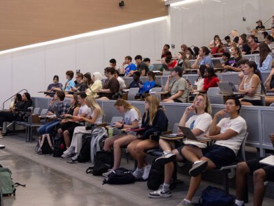 Wide shot of a female KU professor standing in front of a class in a lecture hall on campus.