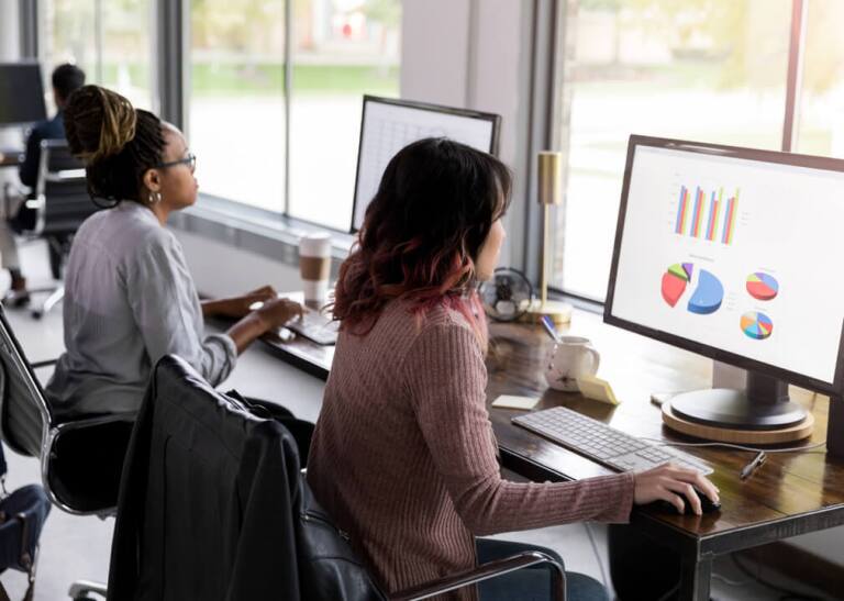 Women on desktop computers looking at graphs