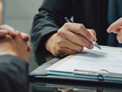 person holding pen and about to sign legal document attached to clipboard