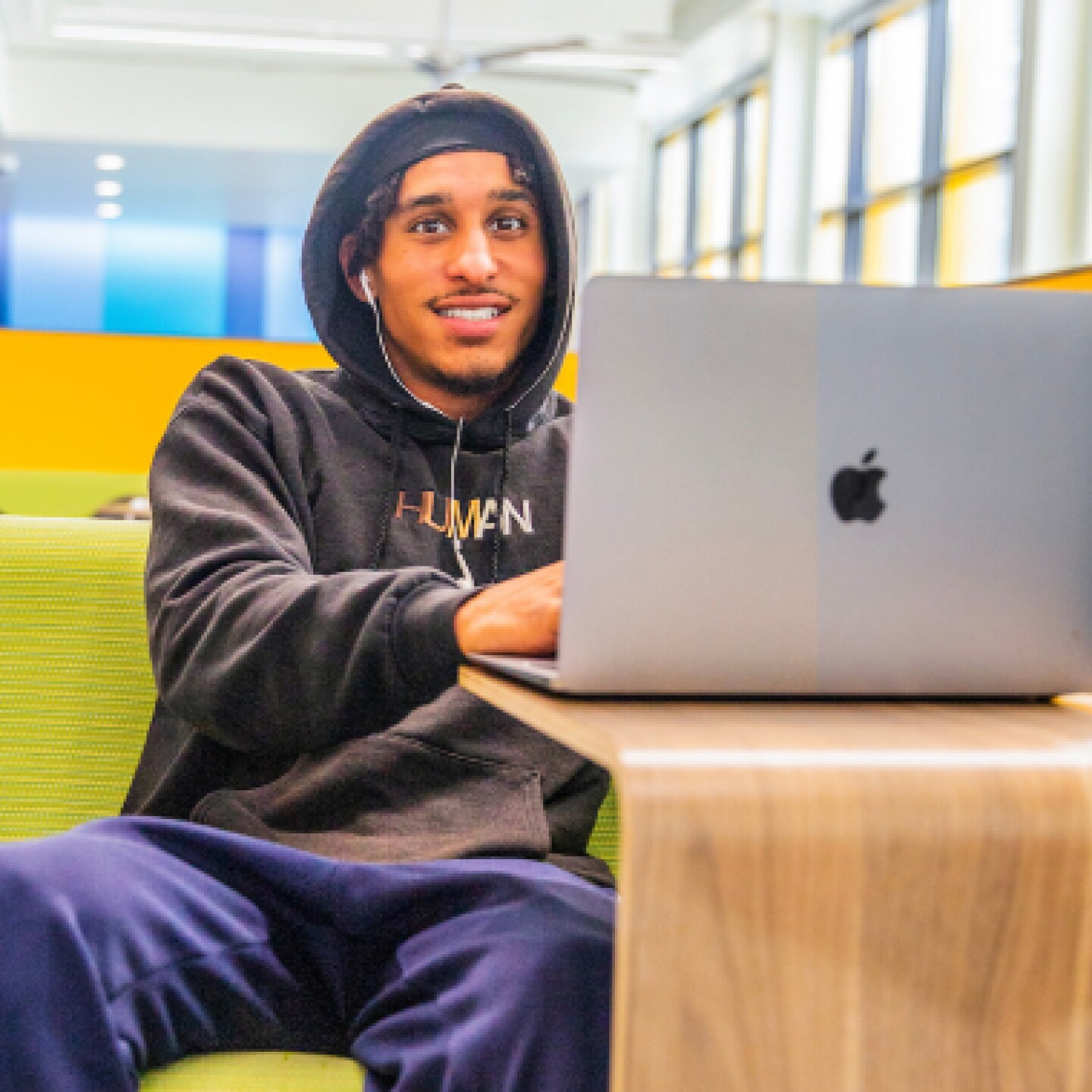 A male CSUMB student sitting on a yellow couch while working on laptop.