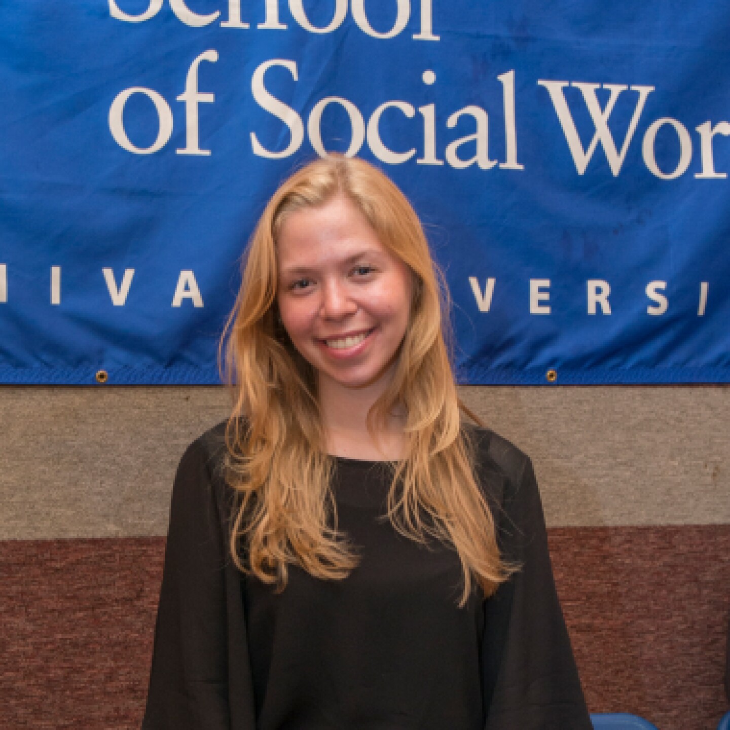 A female Yeshiva University student stands in front of a Wurzweiler backdrop.