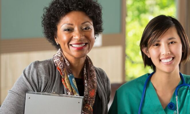 Healthcare administrator holding clipboard standing next to female surgeon wearing stethoscope