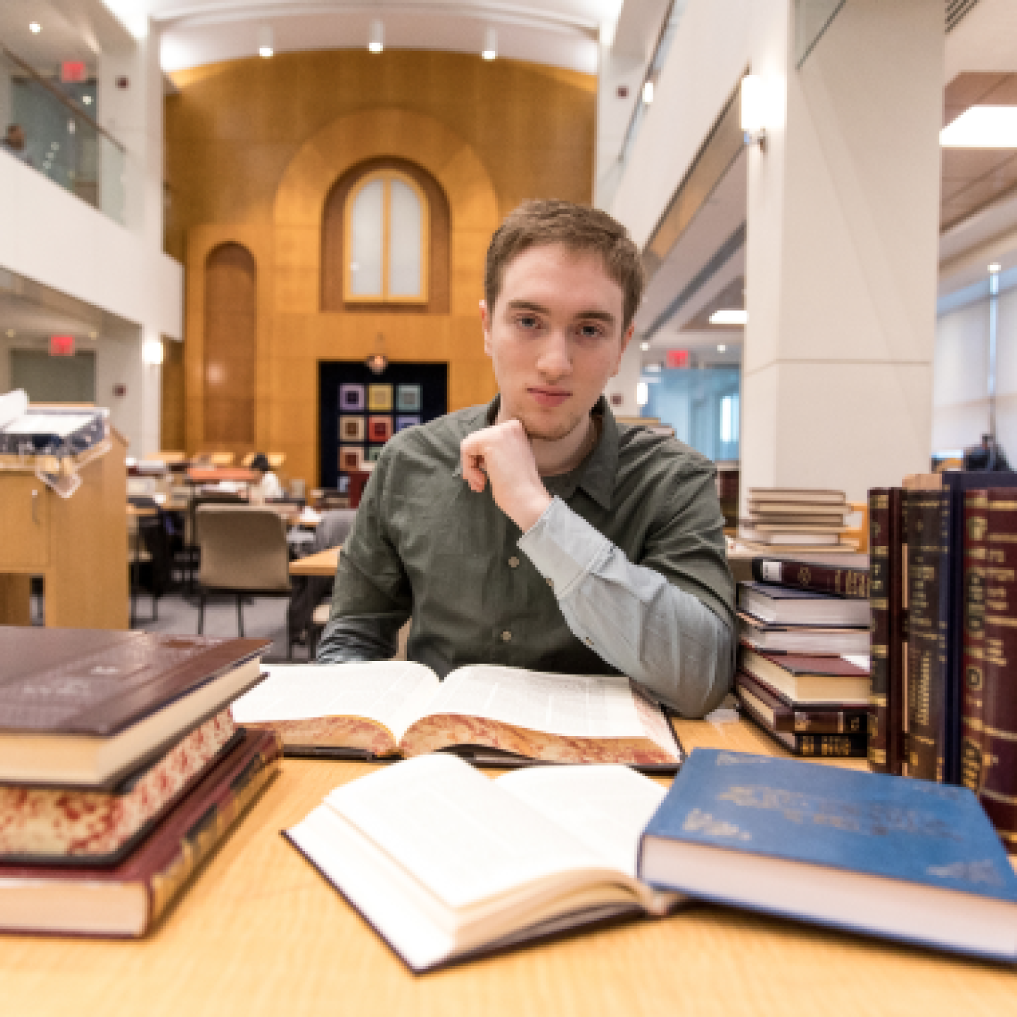 A male Yeshiva University student is sitting in the campus library with books in front of him.