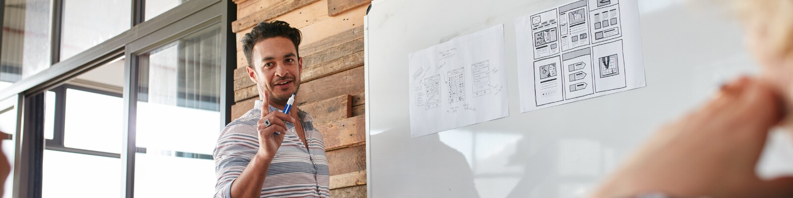 Man stands at cork board walking through wireframes and prototypes models for a group
