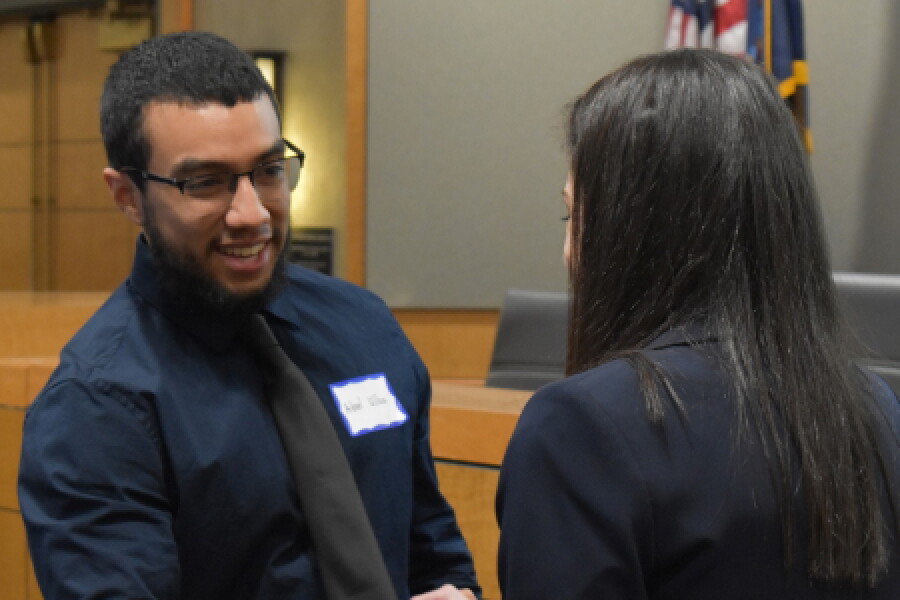 A male and female Hofstra law students conversing in front of a judge's bench.