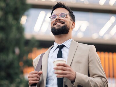 Smiling male attorney holding coffee walking outside office building