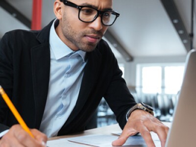 Man with pencil and paper looking at laptop.