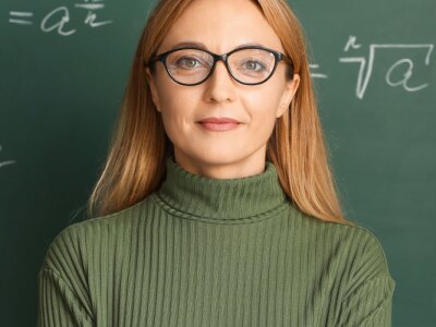 Confident female teacher stands in front of a chalkboard.
