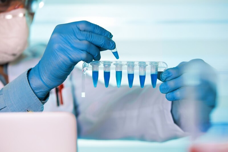 biomedical engineer with blue gloves on dropping liquid into test tubes