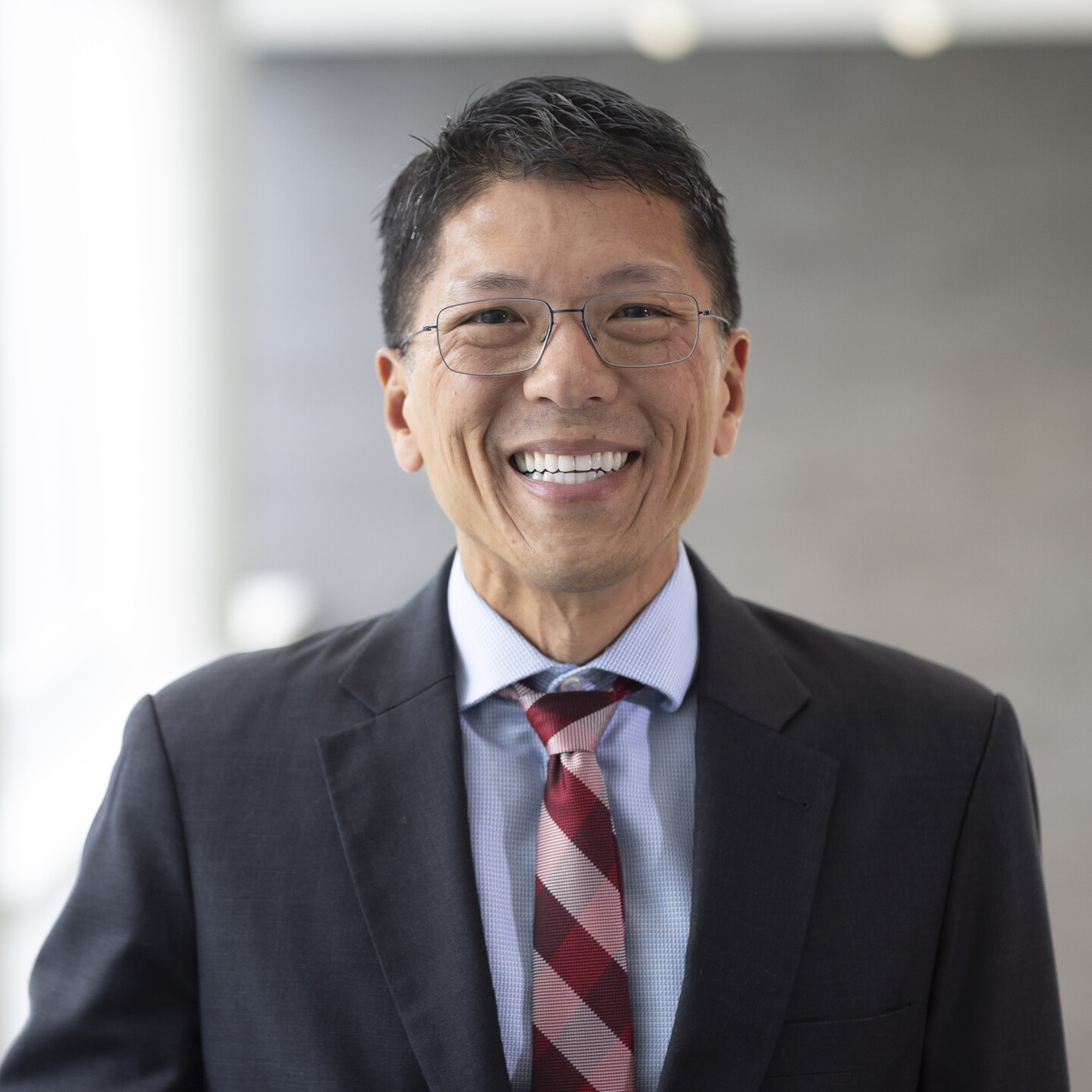 Smiling man with glasses in a dark suit and red tie.