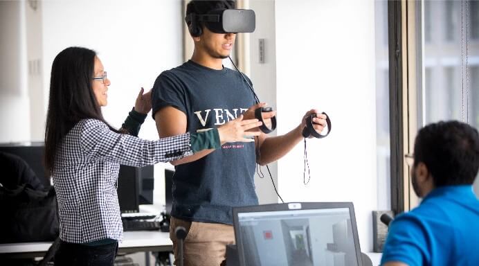 Two students assisting third student using virtual reality equipment
