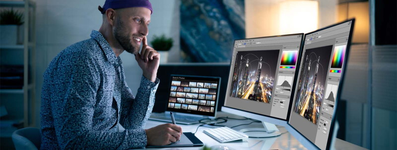 Man sitting at desk, drawing on a tablet while examining his design on multiple screens.