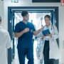 A doctor and a nurse are discussing an upcoming surgery while walking through a busy hospital hallway.