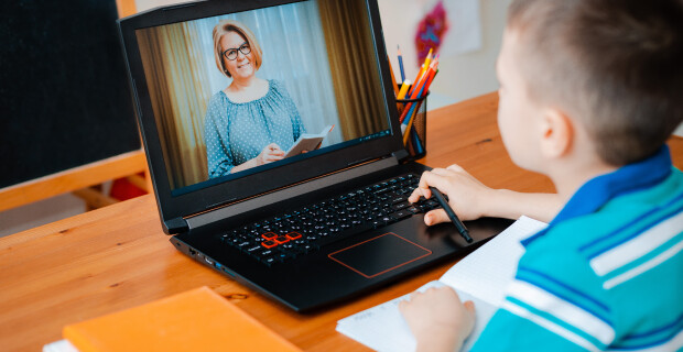 Kid in blue shirt sitting at computer watching teacher