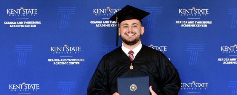 Kent State University graduate in cap and gown holding degree