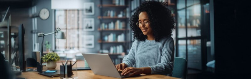 Smiling female of color sitting at a desk in a her home using a laptop