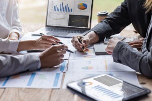 Group of confident business people point to graphs and charts to analyze balance sheets.