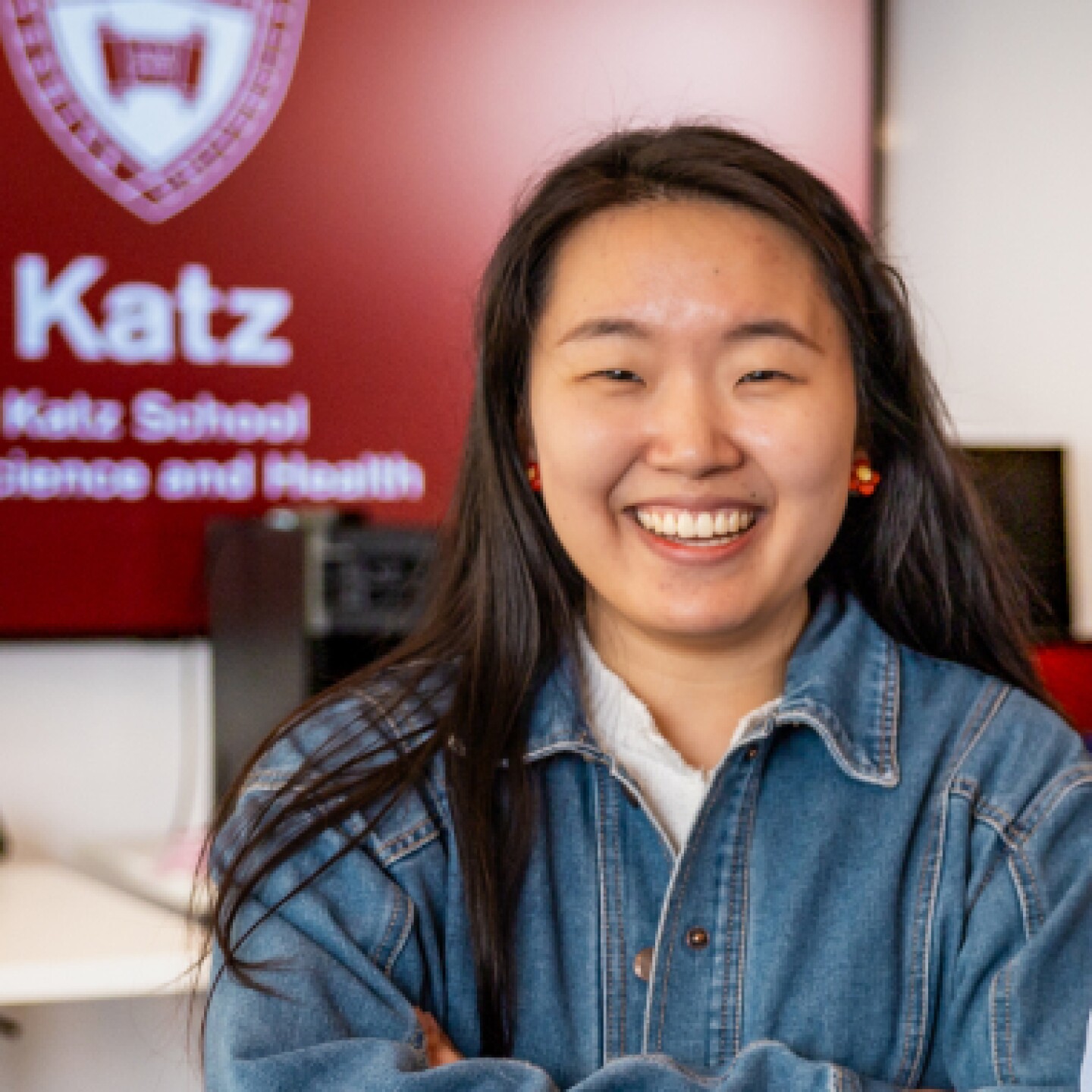 A young female Yeshiva University student stands in front of the Katz logo displayed on a monitor.
