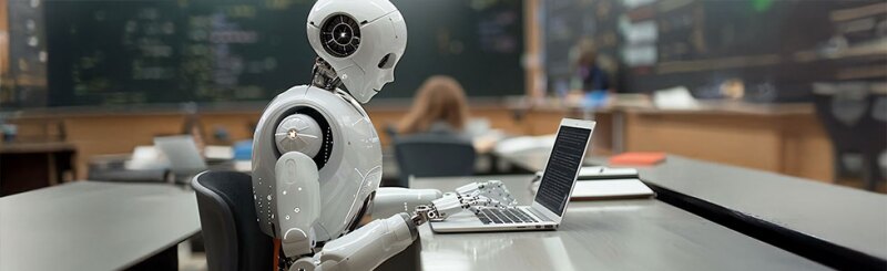Humanoid robot using laptop at a desk In classroom