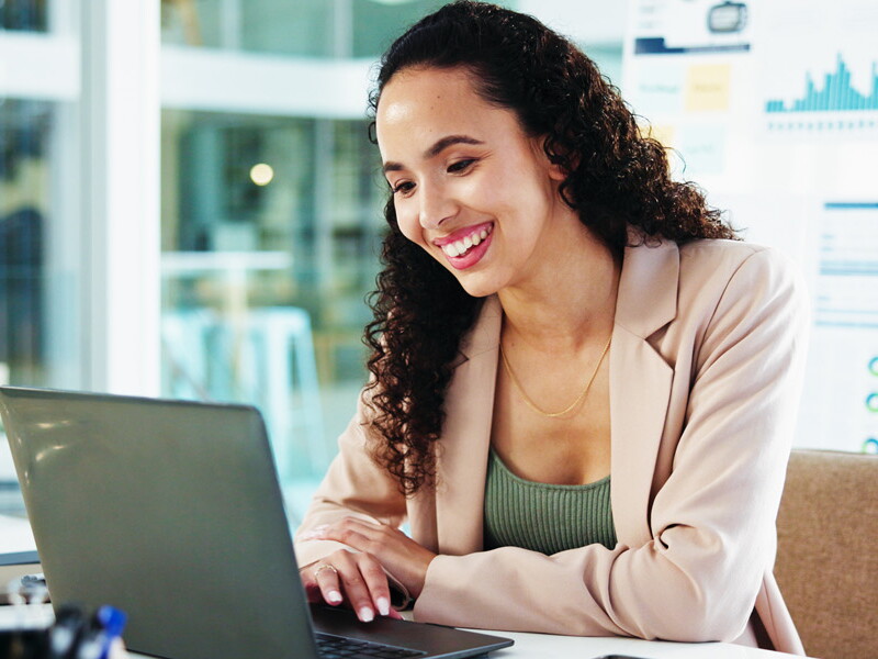 A businesswoman smiles as she sits at her laptop, working in her accounting job.