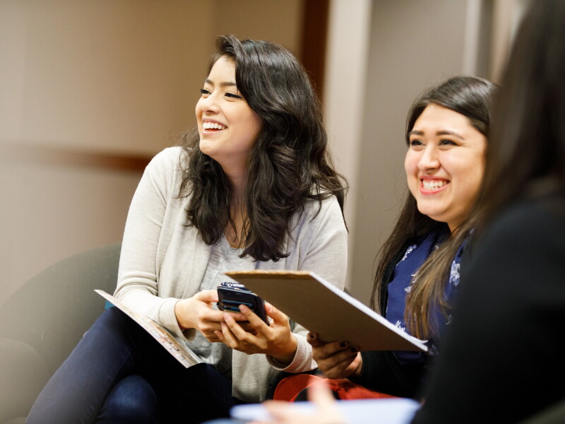 Two women laughing in an office space with notebooks in their hands