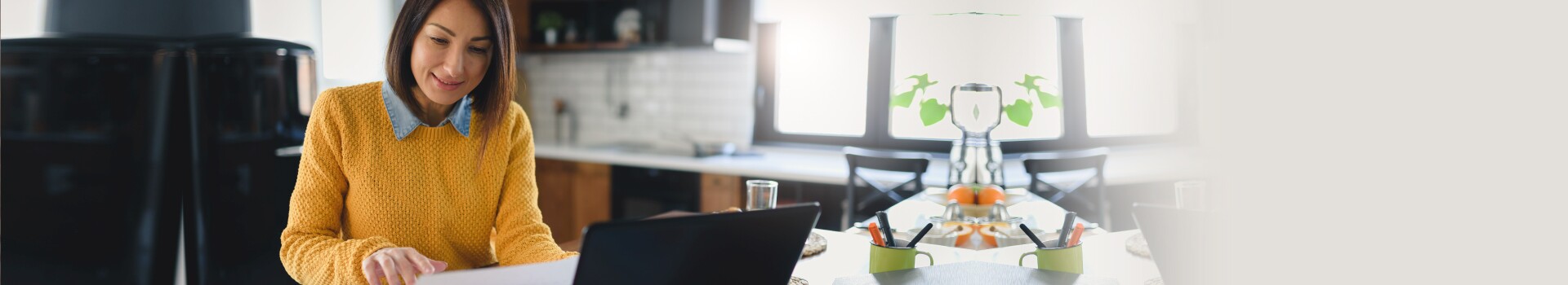 Woman sits in kitchen working on laptop