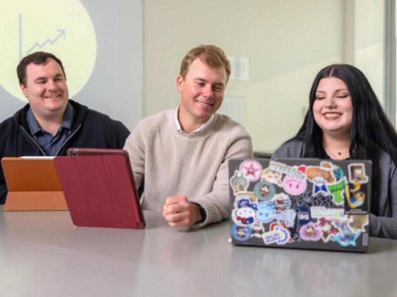 Two male and female CSUMB student smile while viewing laptop screen.