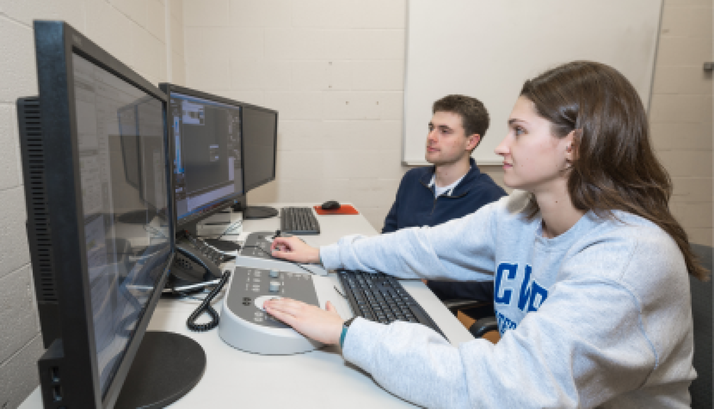 A female CWRU student reviewing software on computer with a male student.
