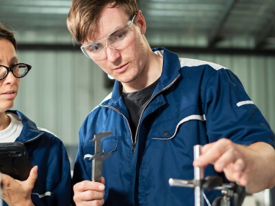 Two mechanical engineers examine a component using precision measuring tools.