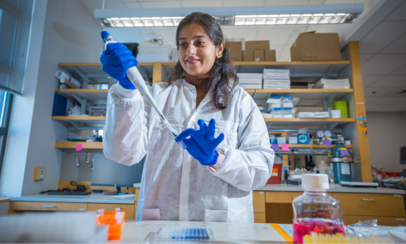 Woman in protective coat and rubber gloves using large syringe to transfer liquid to test tube