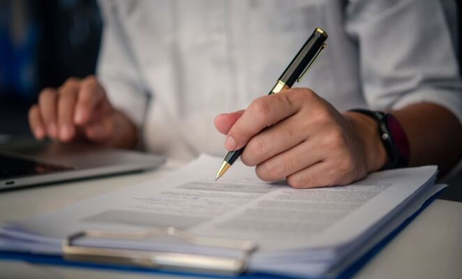 Close up of hand filling out forms on clipboard