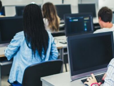 five-people-sitting-at-black-computers-facing-away-from-camera-in-three-rows
