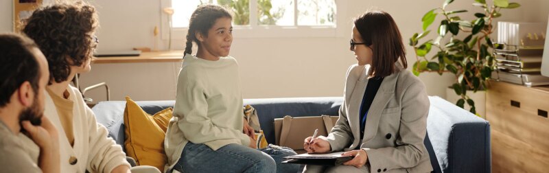 Social worker talking to teenage girl while they sitting on sofa in the living room with foster parents.