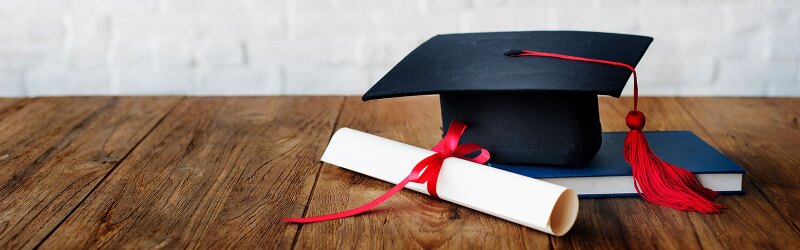 Graduation cap and diploma laying on top of a wooden table