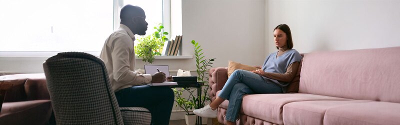 male counselor taking notes in session with female patient sitting on pink couch