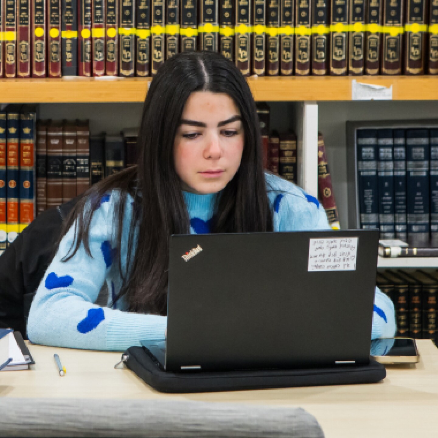A female student works on her laptop while sitting in the campus library.