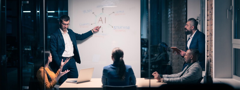 Marketing professionals in a meeting room at a table and a whiteboard with 'AI' written on it.