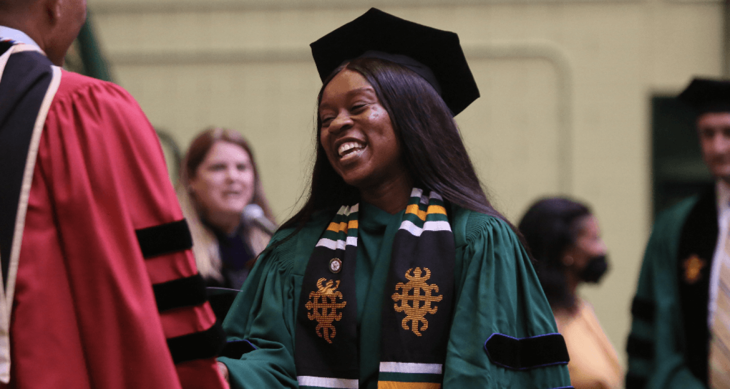 Smiling William & Mary Law School graduate in cap and gown shaking hands with faculty
