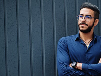 Bearded man in glasses and a blue shirt stands with his arms folded across his chest