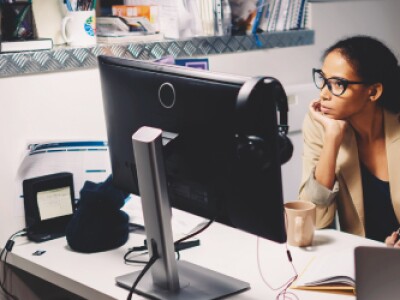 Woman in glasses seated at office desk looking at monitor