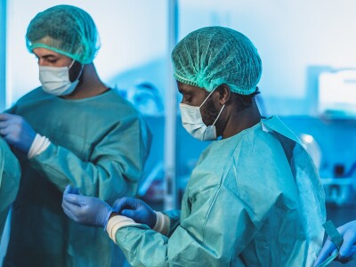 Four hospital staff members help each other put on their personal protective equipment.
