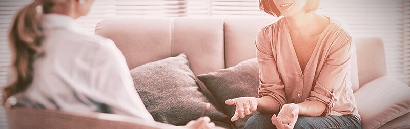 Two women sit facing each other and talking in a counselor's office.