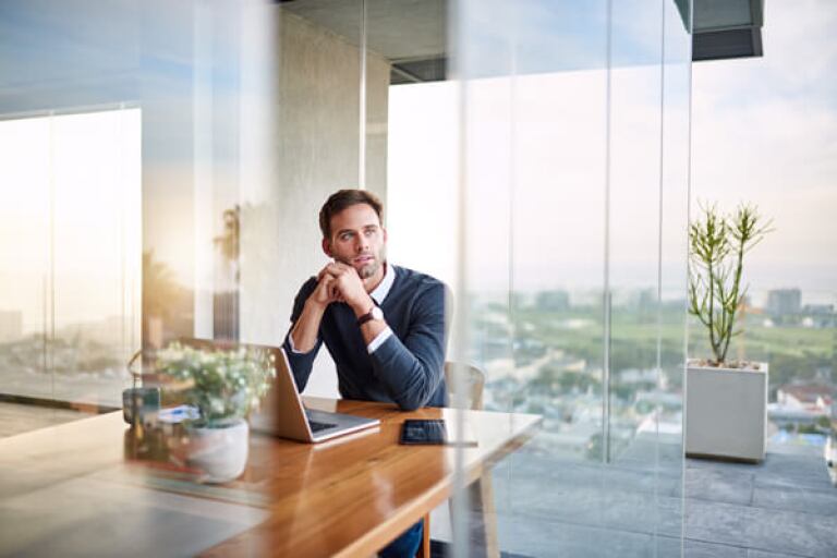Man sitting at table with laptop in front of a large window
